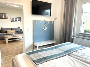 Une chambre à coucher avec un lit, un téléviseur fixé au mur, une table de chevet et une vue sur l’extérieur par une fenêtre.