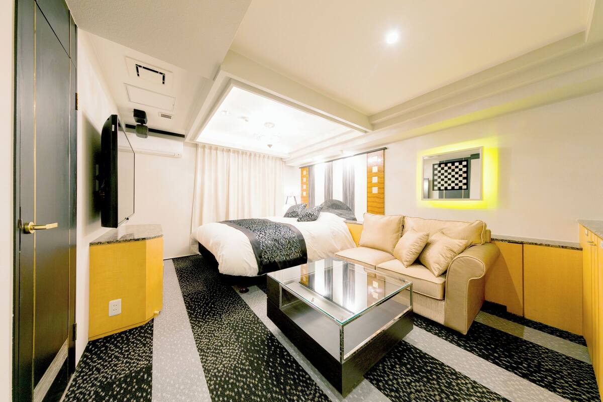A hotel room with a bed, a sofa, a glass coffee table, and a TV.