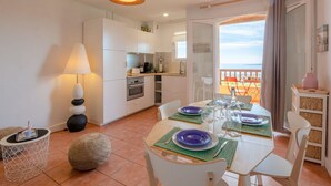 Een moderne keuken met witte kastjes, een eethoek met een tafel gedekt voor twee personen, en een balkon met uitzicht.