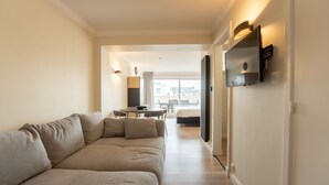 A modern living room with a sofa, a dining table, and a TV mounted on the wall.