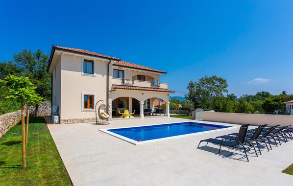 Una casa a due piani con piscina e area relax all'aperto.