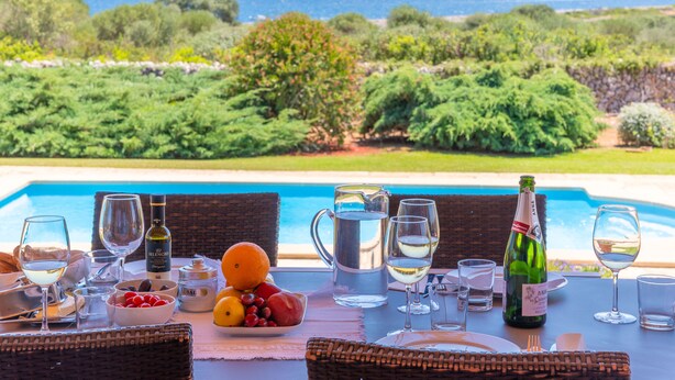 Une table à manger avec vue sur la mer, une bouteille de vin et une carafe d’eau.