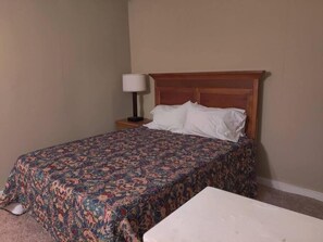 Een hotelkamer met een bed, een nachtkastje met een lamp en een kleine witte tafel.