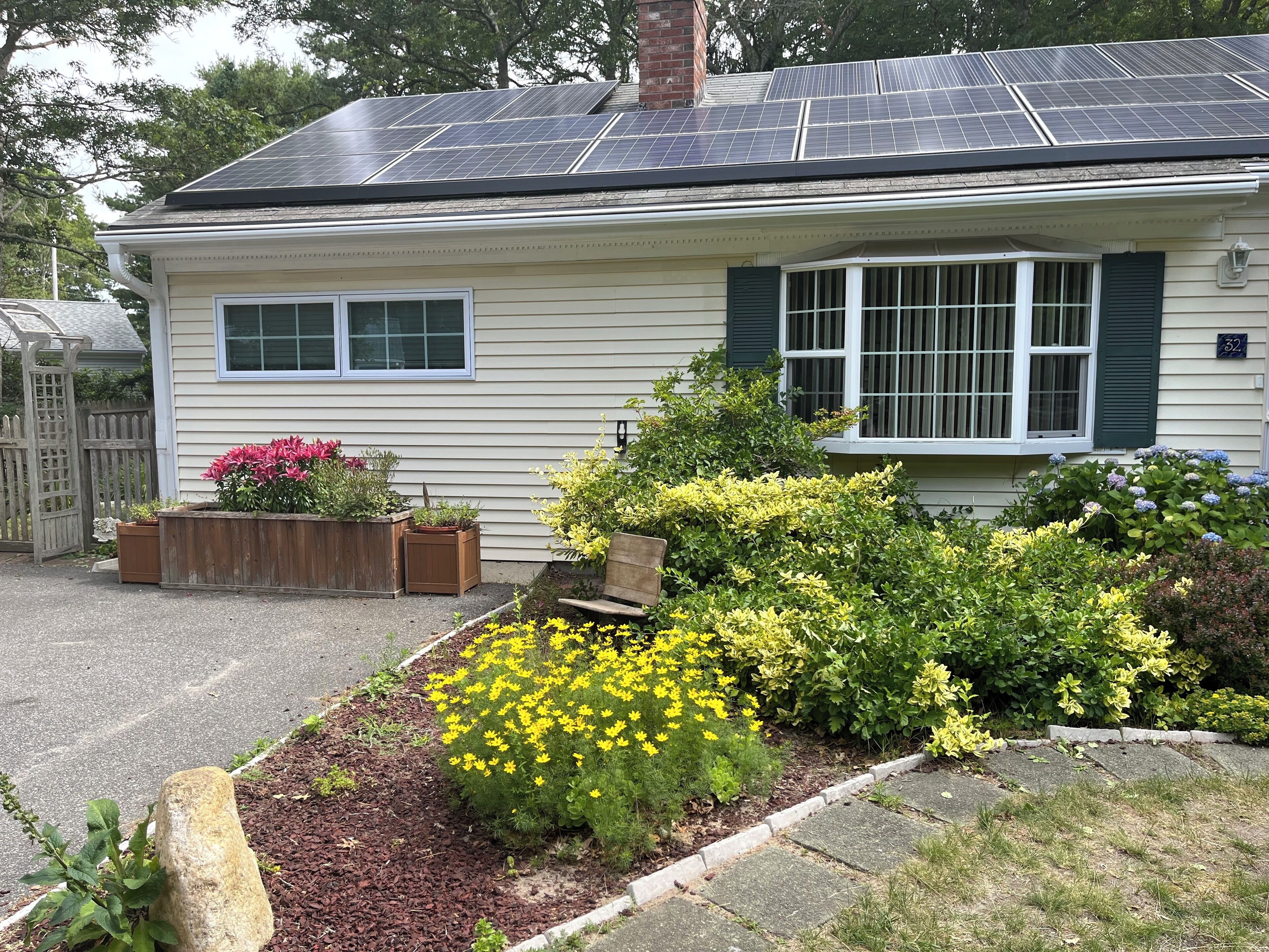 A house with solar panels on the roof, a front porch, and a garden with various plants and flowers.