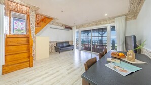 Amplia sala de estar con una escalera de madera, un sofá, una mesa de comedor con sillas y un ventanal con vistas al exterior.