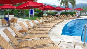 Ein Poolbereich mit Korlounge-Stühlen und roten Sonnenschirmen, freie Sicht auf den Pool und eine tropische Landschaft im Hintergrund.