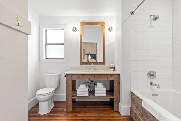 A bathroom with a wooden vanity, a toilet, a sink with a mirror, and a bathtub.