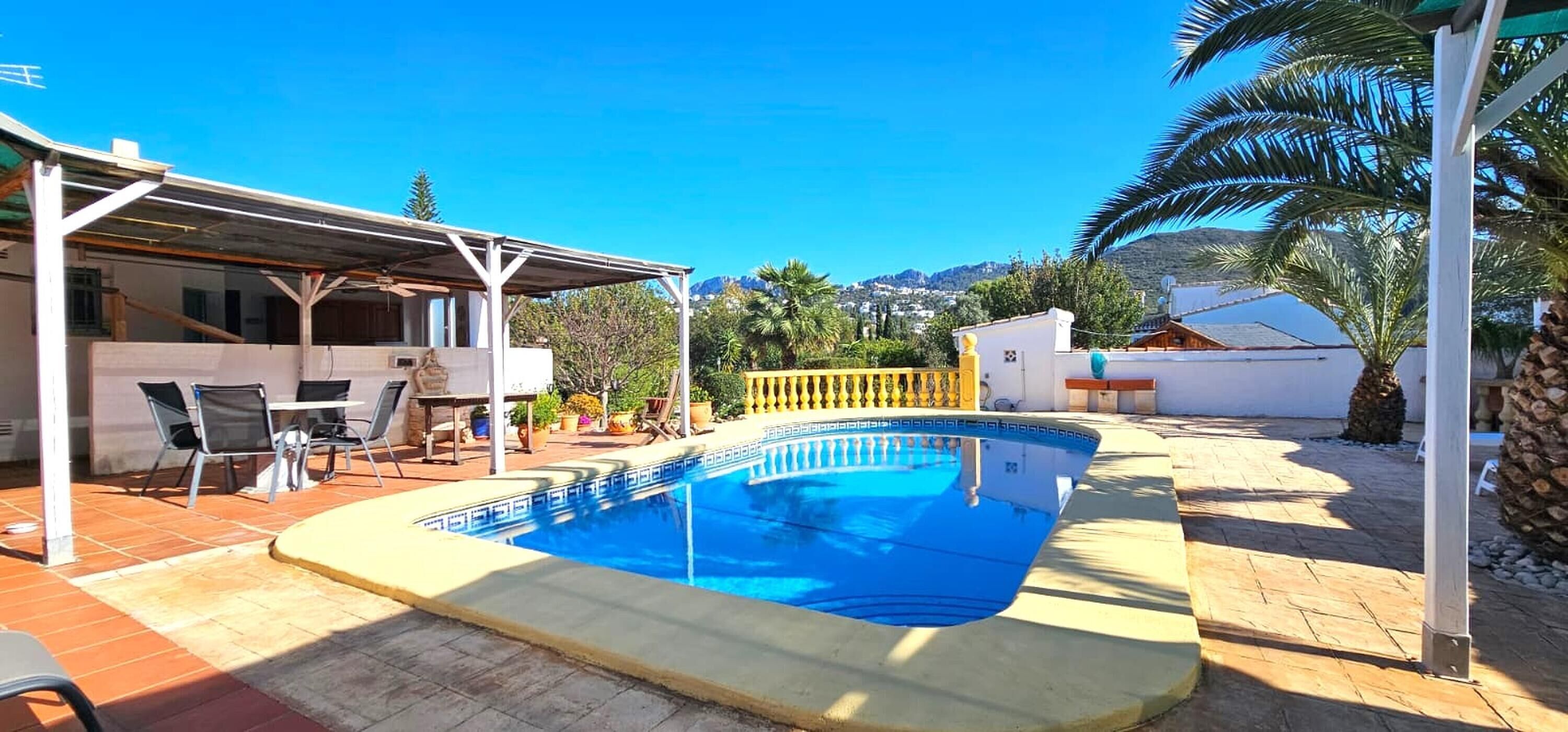 Une piscine avec un patio couvert, un espace salon extérieur et une vue sur un paysage montagneux.