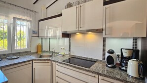 A modern kitchen with white cabinets, a granite countertop, a built-in stove, a coffee maker, and a window with a view of greenery. - Villa LOS JAZMINES at Monte Pego (Pego)