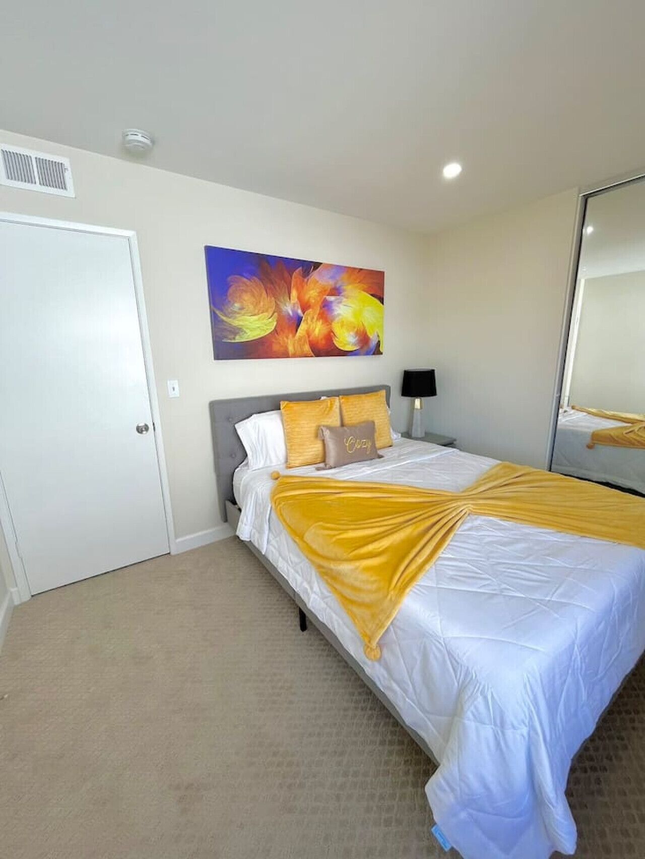A hotel room with a bed, a painting, a door, and a mirror.