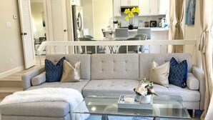 A modern living room with a grey sectional sofa, a glass coffee table, and a blue patterned rug. - Family Paradise near Disneyland w/ Sparkling Pool (Fountain Valley)
