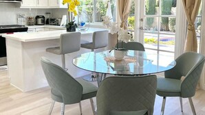 A modern kitchen with white cabinets, a central island, and a dining area with a glass table and four chairs. - Family Paradise near Disneyland w/ Sparkling Pool (Fountain Valley)