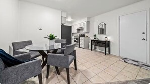 A modern kitchen with white cabinets, a central island, and a dining area with a glass table and grey chairs.