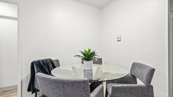A round glass table with four grey upholstered chairs, a potted plant, and a white vase.