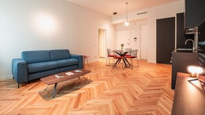 Uma sala de estar moderna com um sofá azul, uma mesa de centro de madeira e um espaço de jantar com uma mesa redonda e cadeiras.