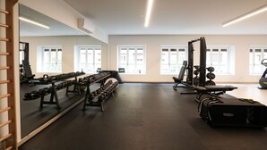 Uma academia com equipamentos de ginástica, amplas janelas e um espelho.
