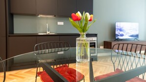 Uma cozinha moderna com armários escuros, uma mesa de jantar de vidro e cadeiras de metal, e um vaso com tulipas na mesa.