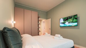 Quarto bem arrumado com cama, almofadas, guarda-roupa e televisão exibindo uma paisagem natural.