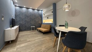 A modern room with a wooden floor, a sofa, a round table with chairs, a TV on a cabinet, and a patterned wall. - Torino, Tesoriera apartment (Torino)