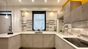 A modern kitchen with a central island, built-in appliances, and a window with decorative curtains. - Torino, Tesoriera apartment (Torino)