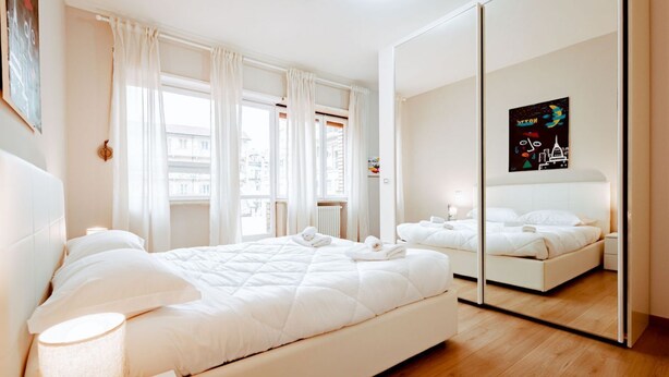 A modern hotel room with a large bed, a bedside table with a lamp, a mirror, and a cityscape artwork on the wall. - Torino Centro, Repubblica Apartment (Torino)