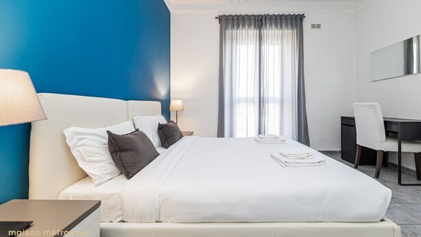 A hotel room with a bed, a desk, a chair, a lamp, and a window with curtains.