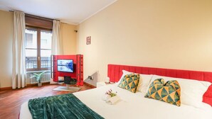 Ein Hotelzimmer mit einem großen Bett, einem Fernseher, einem roten Kopfteil und einem Fenster mit Vorhängen.