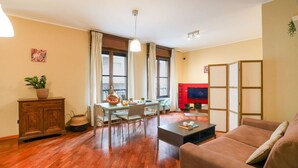 Ein Wohnzimmer mit einer Couch, einem Couchtisch, einem Esstisch mit Stühlen, einem Fernseher und einem Schrank.