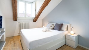 A bedroom with a sloped ceiling, a large window, a white bed, and a bedside table with a lamp. - Torino Centro, Art House Arsenale (Torino)