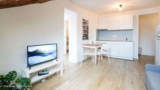 A modern living room with a flat-screen TV, a dining area with a white table and chairs, and a kitchen with white cabinets and a wooden floor. - Torino Centro, Art House Arsenale (Torino)