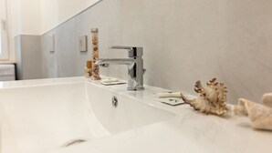 Une salle de bain moderne avec un grand lavabo blanc, un robinet chromé et un bocal en verre contenant des objets décoratifs.