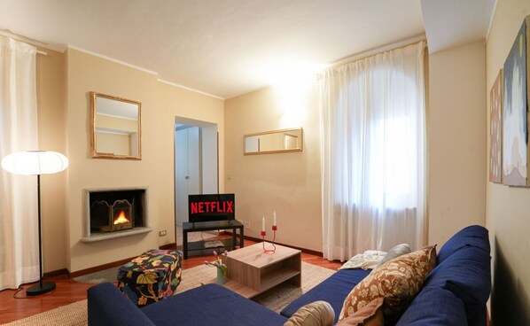 A cozy living room with a fireplace, a sofa, a coffee table, and a TV displaying 'NETFLIX'.