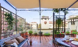 A covered patio with a table set for dining, potted plants, and a bench.