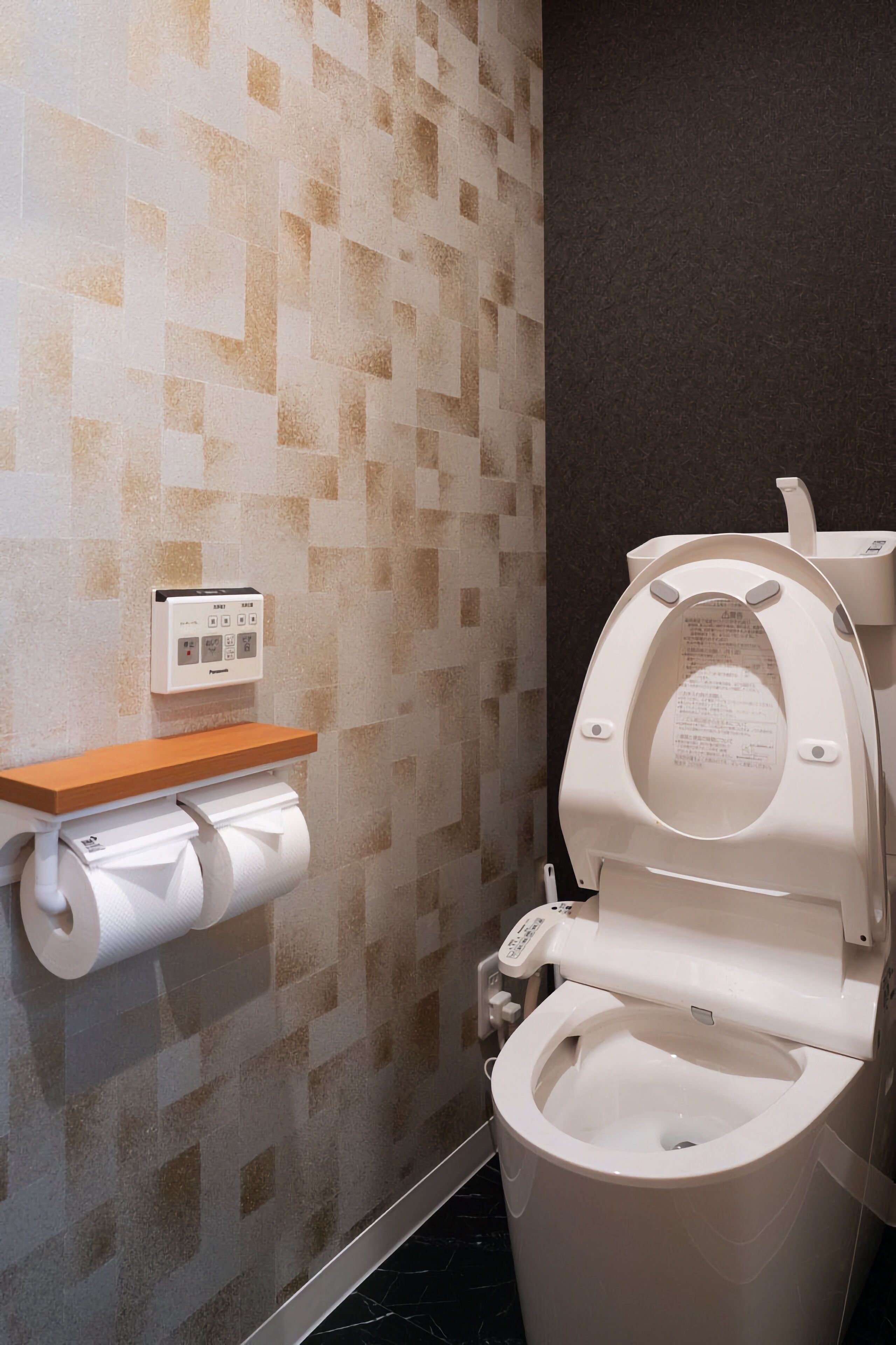 A modern bathroom with a toilet, a toilet paper holder, and a control panel on the wall.
