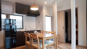 A compact kitchen with a dining area, including a wooden table and chairs, a microwave, and a stove. - HANASTAY YANAGI (Osaka)