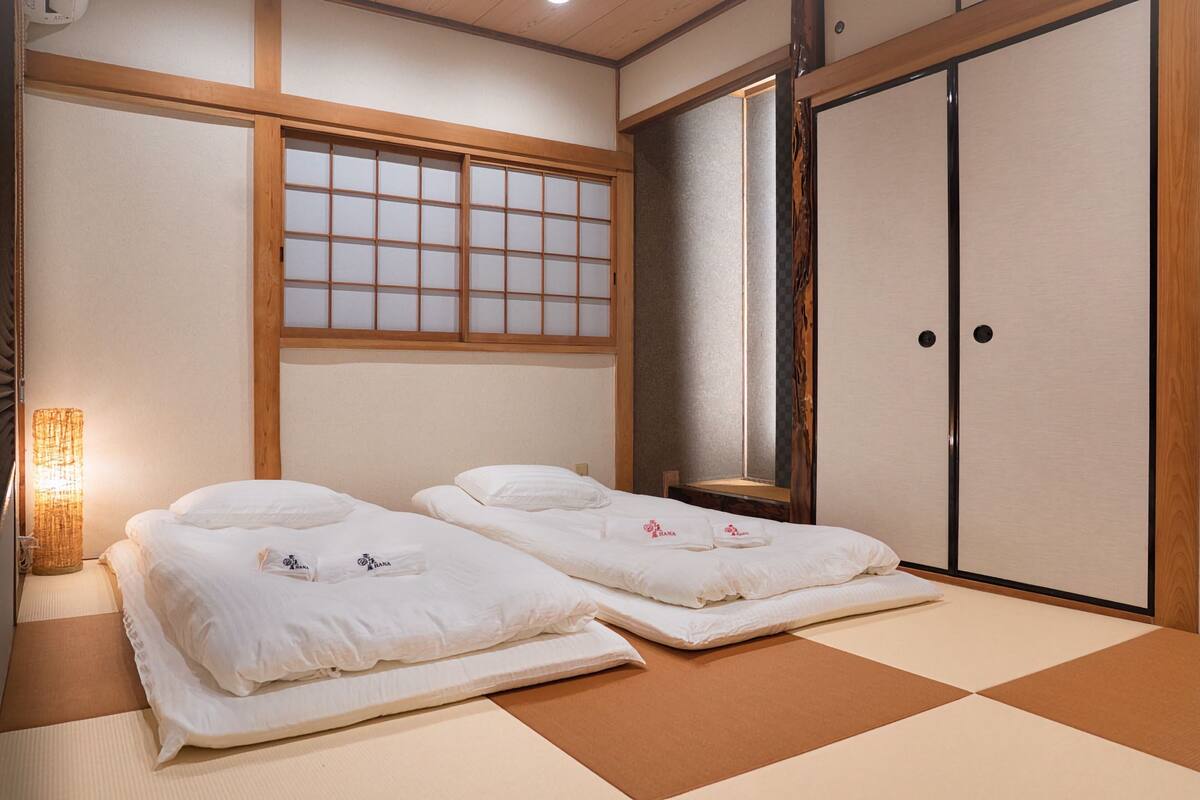 A traditional Japanese room with tatami flooring, two beds with white bedding, a shoji screen, and a sliding door.