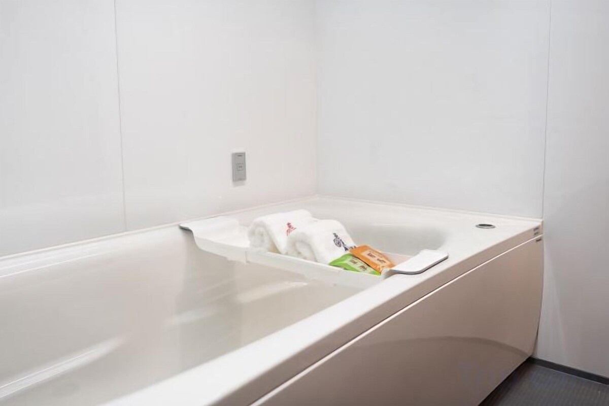 A white bathtub with a towel and a bottle of shampoo.