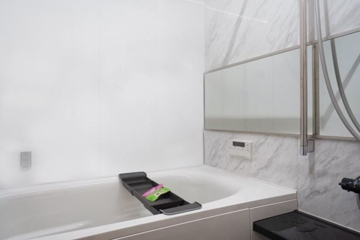 A modern bathroom with a white marble wall, a black bathtub, and a mirror with a metallic frame.