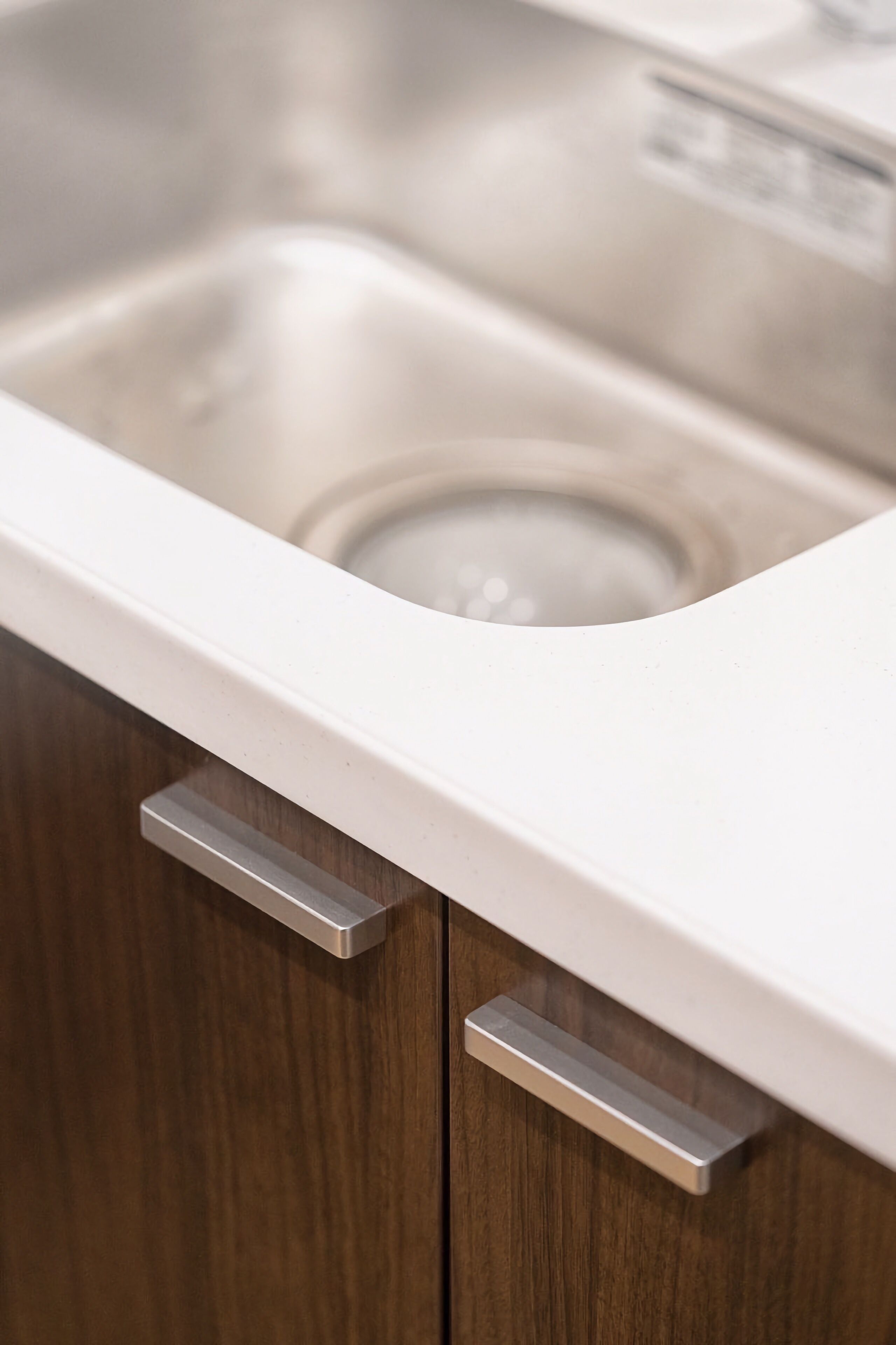A stainless steel sink with a white countertop and wooden cabinet doors.