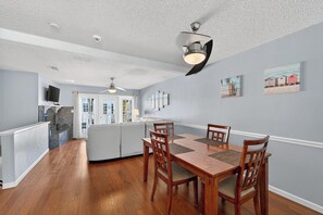 Un coin repas avec une table et des chaises en bois, un ventilateur de plafond et des œuvres d’art accrochées au mur.