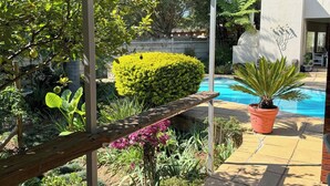 A poolside area with a wooden deck, a potted plant, and a well-maintained garden with various plants and flowers.