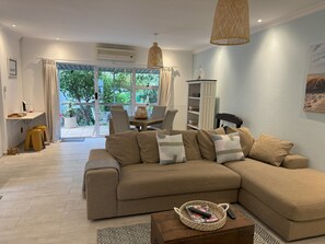 Relax in this inviting living room with a large sofa, wooden coffee table, and a view of lush greenery outside.