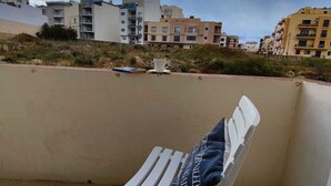 En vit plaststol med en kudde på en balkong med utsikt över ett bostadsområde med flera hyreshus.