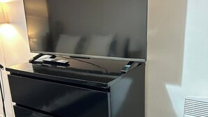Un téléviseur à écran plat, posé sur un support noir, avec une télécommande, le tout placé devant un mur blanc.