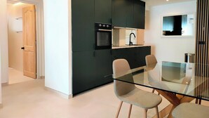 Een moderne keuken met donkere kastjes, een glazen eettafel en twee stoelen.