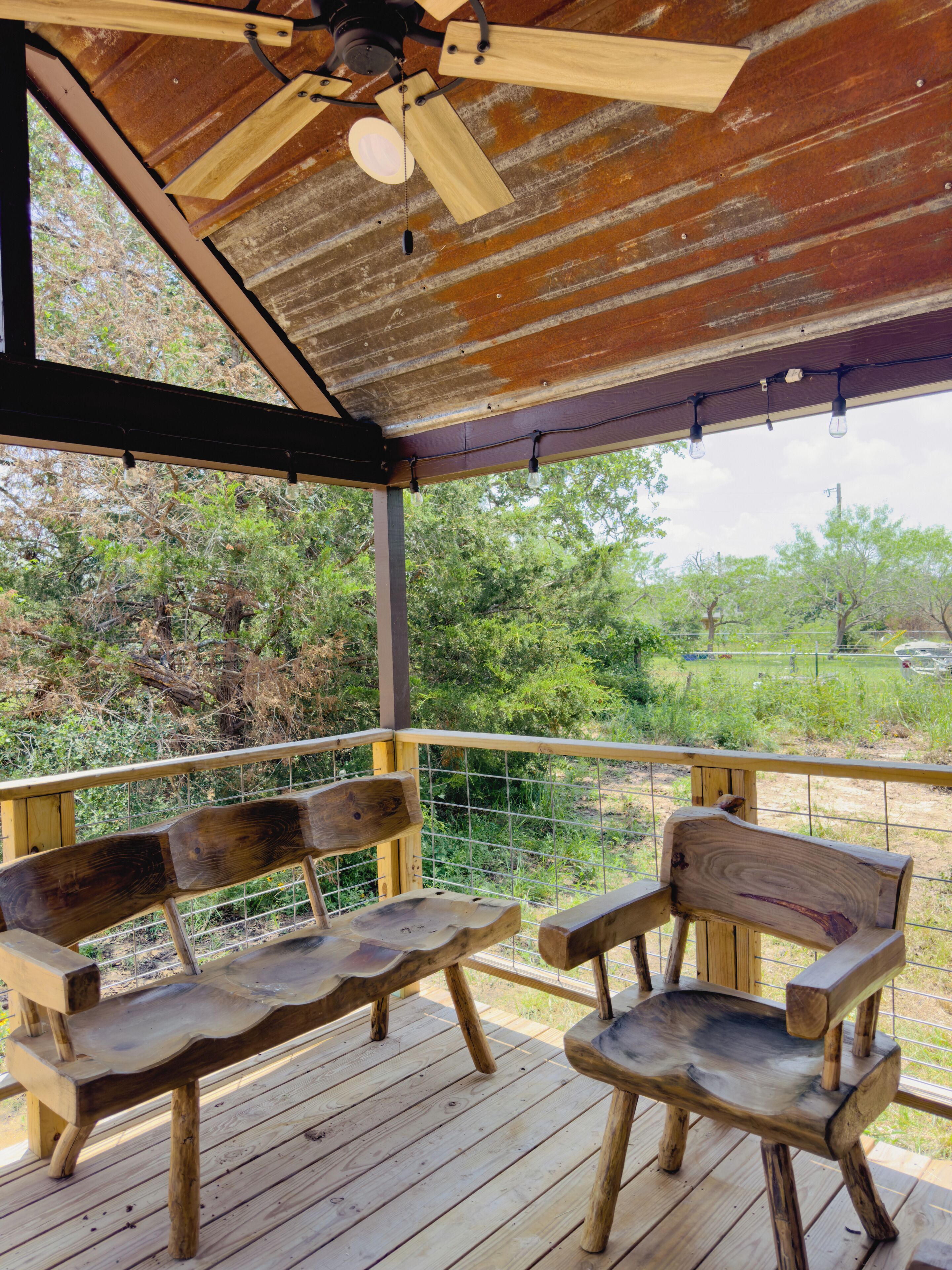 A wooden deck with two benches and a ceiling fan.