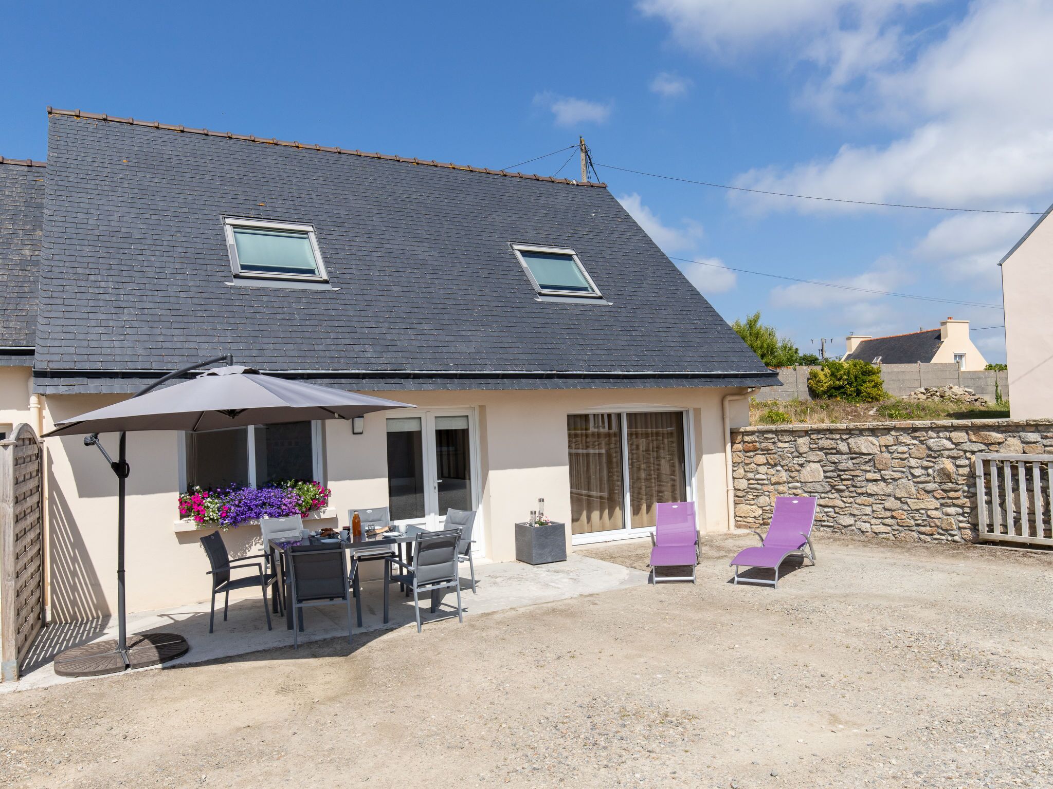 A house with a patio area featuring a table and chairs, a covered seating area with a table and chairs, and a stone wall.