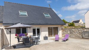 A house with a patio area featuring a table and chairs, a covered seating area with a table and chairs, and a stone wall. - La Roselière by Interhome (Guissény)