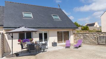 A house with a patio area featuring a table and chairs, a covered seating area with a table and chairs, and a stone wall.