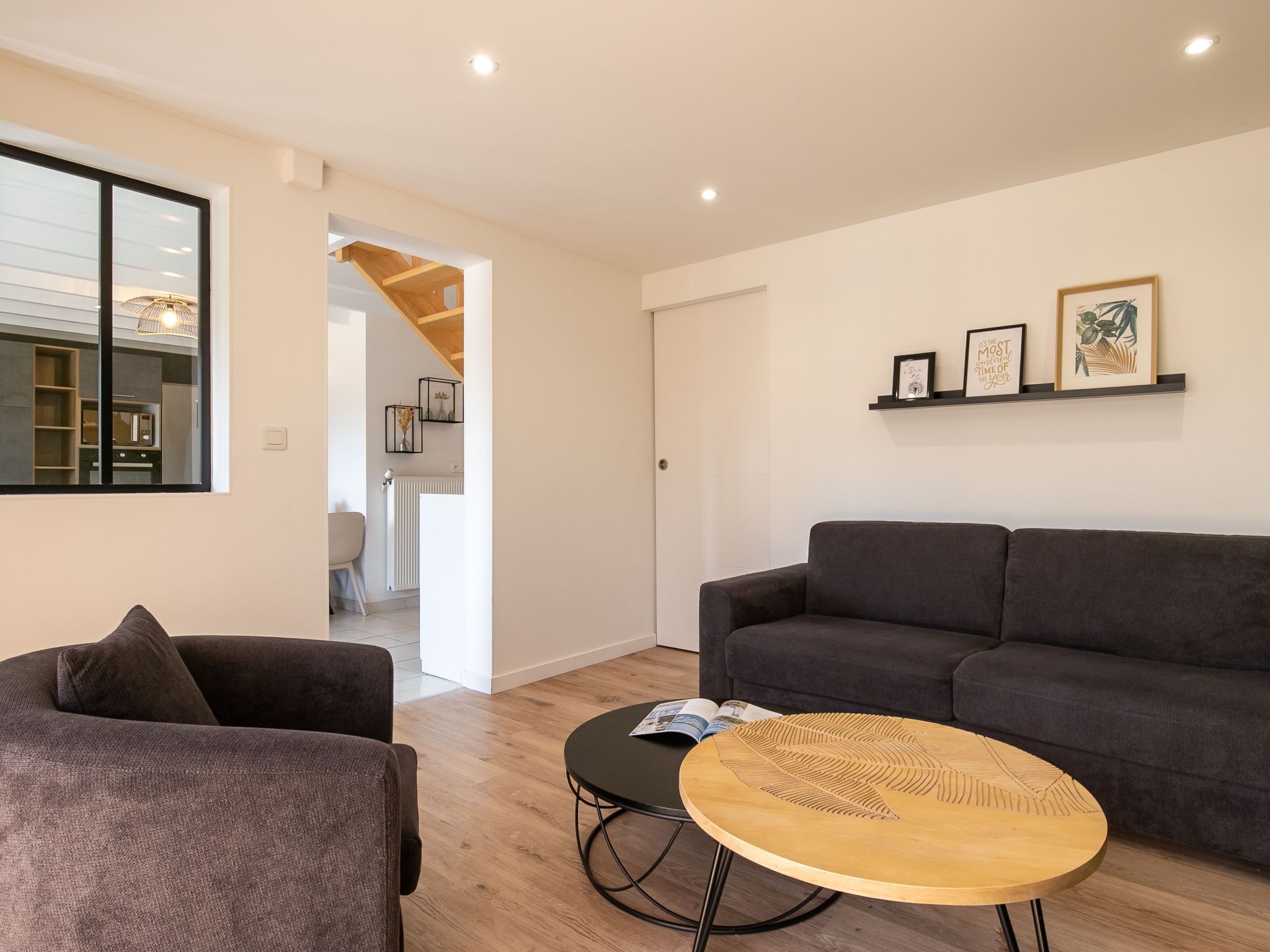 A modern living room with a grey sofa, a round wooden coffee table, and a bookshelf with framed pictures.